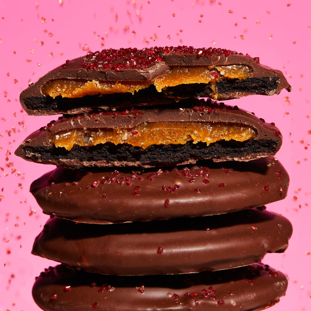 A stack of mini chocolate-covered strawberry snap cookies with strawberry sugar raining down from above