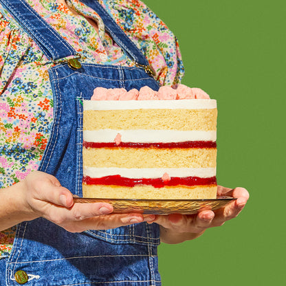 A close up side view of a person carrying a 6 inch strawberry shortcake cake on a glass plate