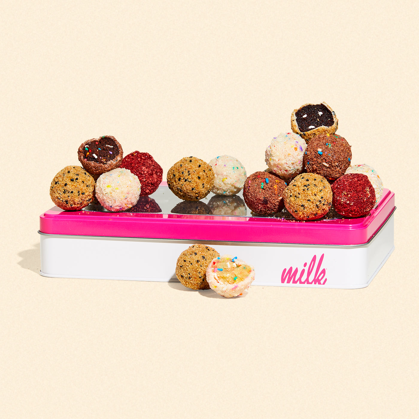 An assorted of 18 unwrapped cake truffles sitting on top of a branded giftable milk bar tin. Flavors include B'day, Chocolate B'day, Red Velvet Cheesecake, and S'mores.