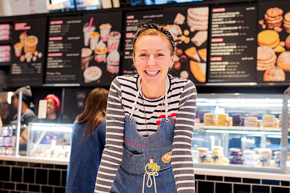 Founder Christina Tosi smiling in front of a giant menu board in the NYC Flagship store.