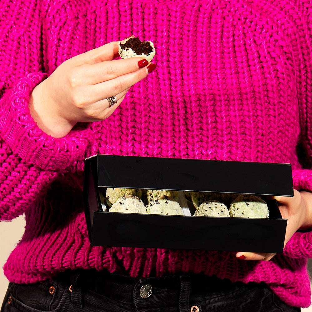 A person presenting a box of limited-edition chocolate mint chip cake truffles.