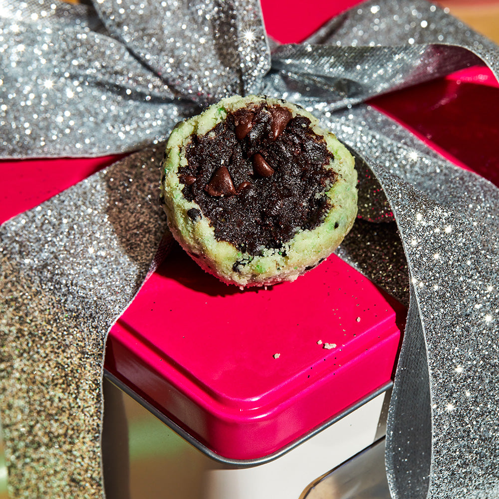 A chocolate mint chip cake truffle split down the middle and sitting on a top of a holiday tin.