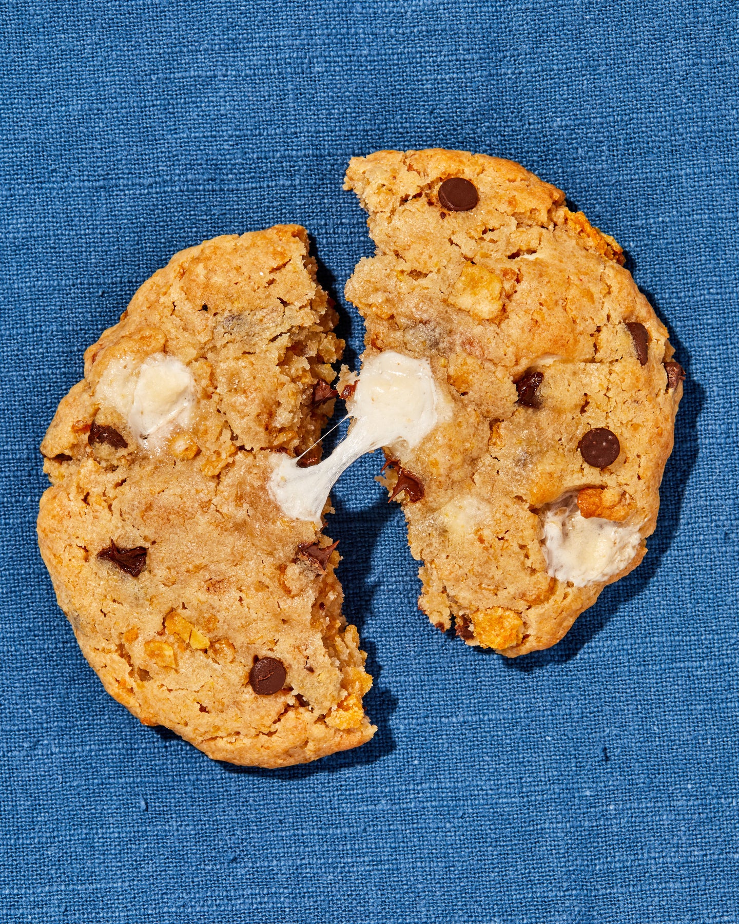 overhead view of a cornflake chocolate chip marshmallow cookie split down the middle with a gooey marshmallow pull 