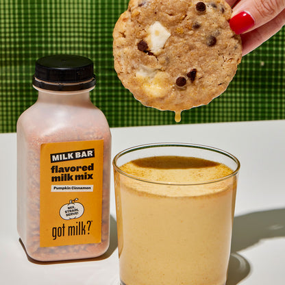 A person dipping a cornflake chocolate chip marshmallow cookie into a glass of freshly made Pumpkin Cinnamon Milk.