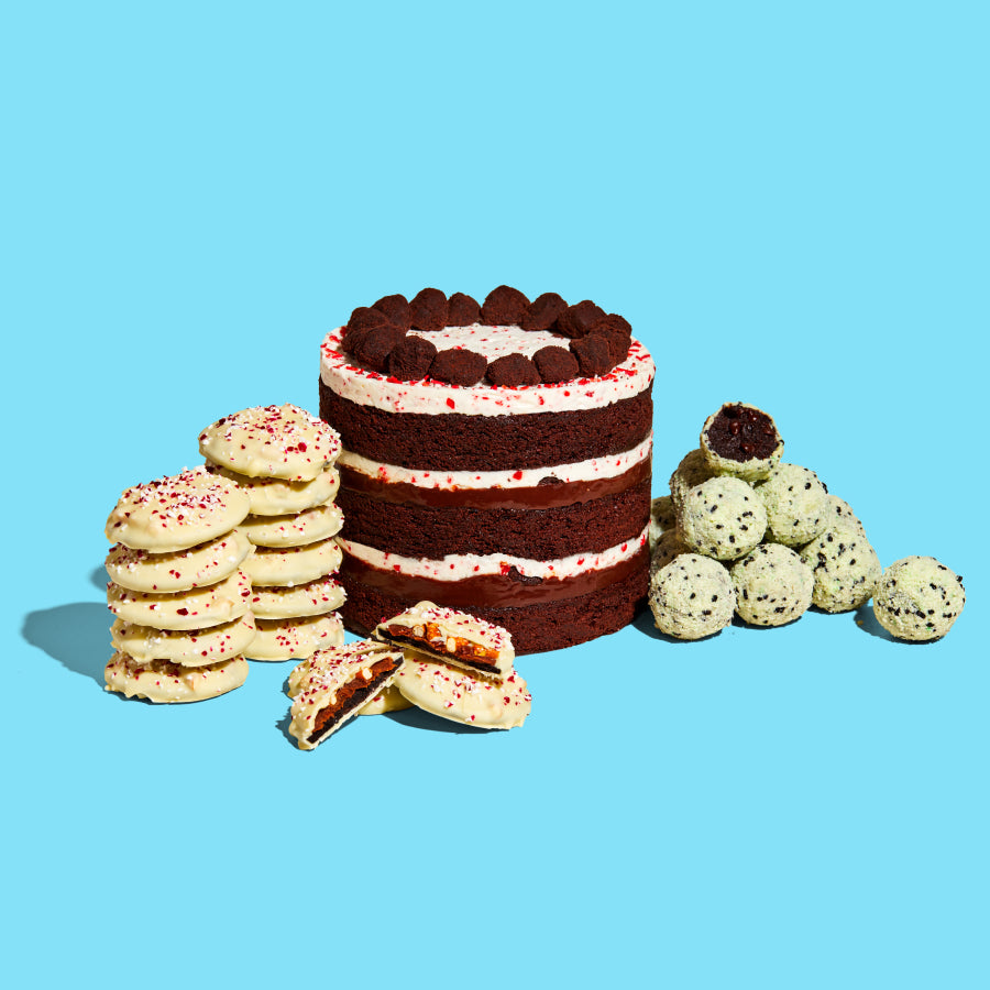 The limited-edition 6" Peppermint Bark Cake, surrounded on both sides by a pile of Mint Chip Cake Truffles, and 2 stacks of Mini Peppermint Snap Cookies.