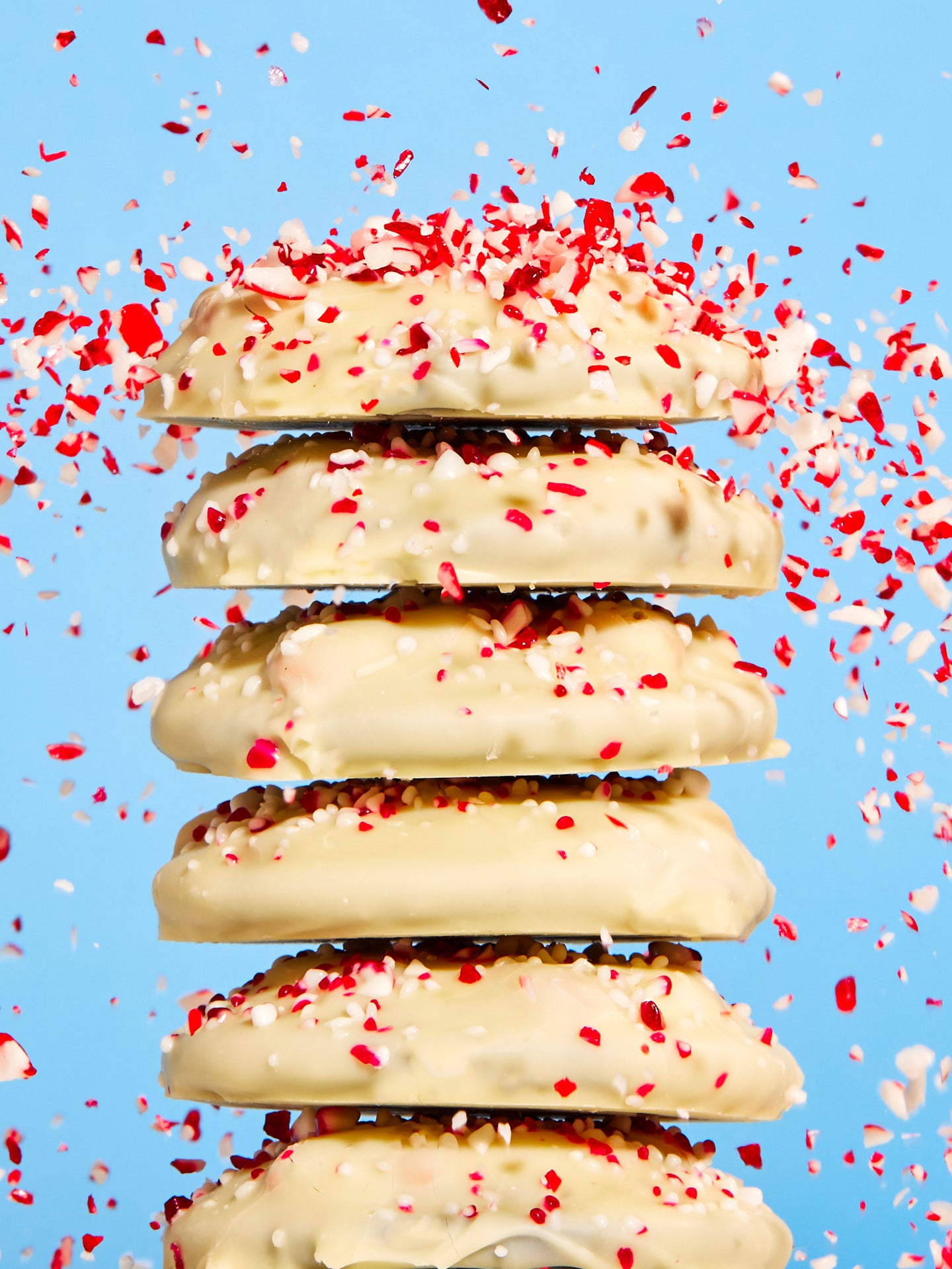 A stack of 6 unwrapped mini peppermint bark snap cookies with candy cane bits raining down.