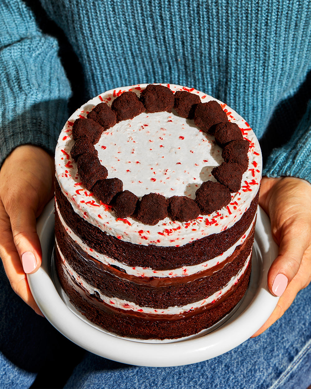 Overhead of the limited-edition Peppermint Bark Cake being presented on a plate by a person. 