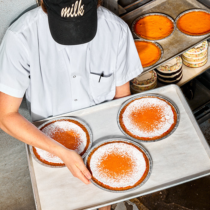 Overhead view of a baker in the kitchen carrying a tray of freshly baked Pumpkin Milk Bar Pies.