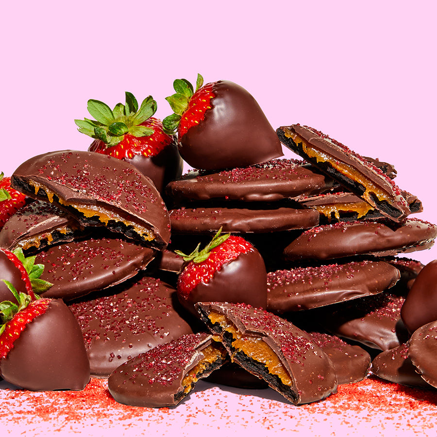 Side view of a large pile of unwrapped mini chocolate-covered strawberry snaps with chocolate covered strawberries mixed throughout.