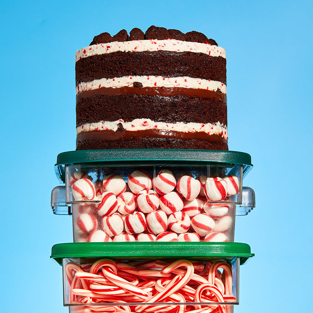 A 6" Peppermint Bark Cake sitting on two stacked containers filled with soft peppermint candies and candy canes.