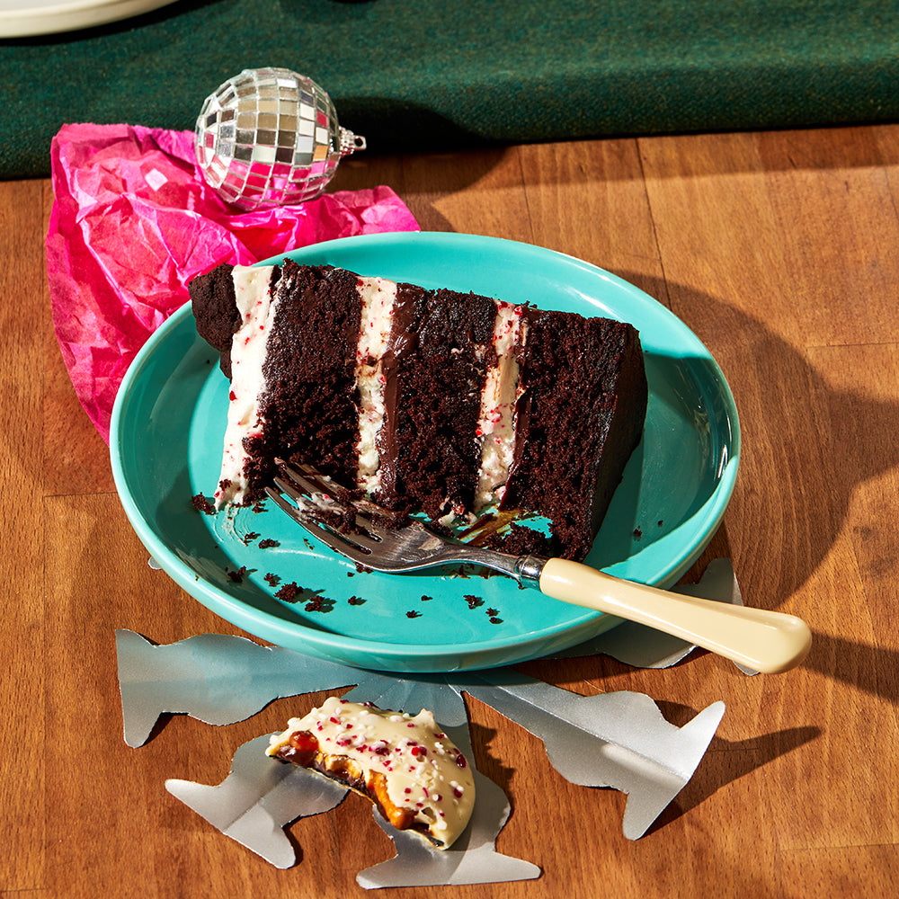 A slice of Peppermint Bark Cake on a table with holiday festive decor.