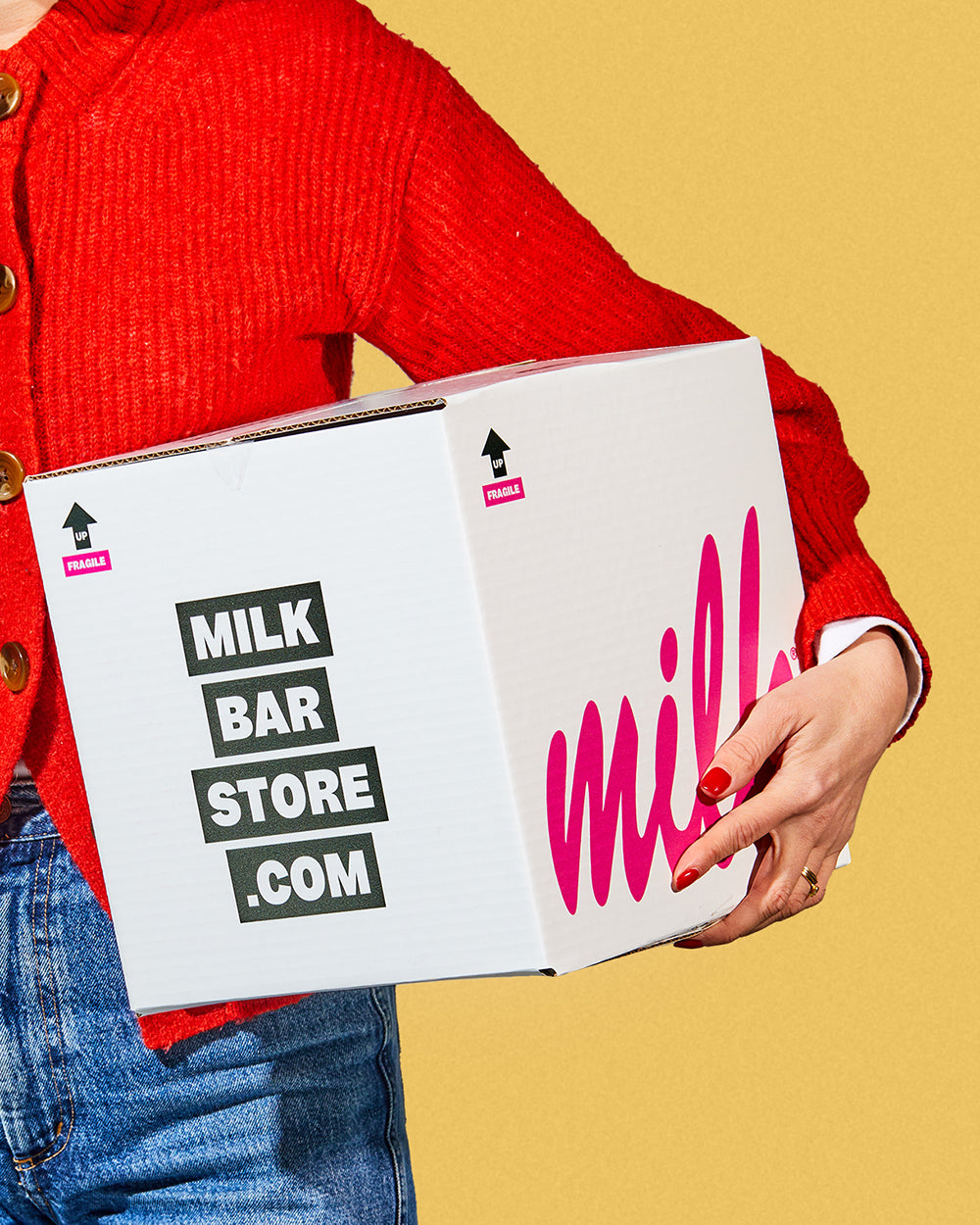 Front view of a branded milk bar shipping box being held in a human's hands and propped up against the side of their torso. Mother's Day treats are delivered nationwide!