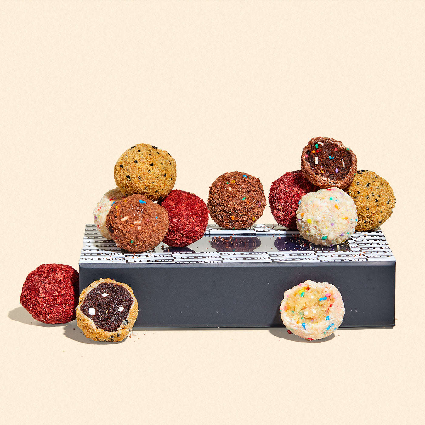 An assortment of unwrapped cake truffles sitting on top of a branded giftable gift box. Flavors include Birthday, Chocolate Birthday, Red Velvet Cheesecake, and S'mores.