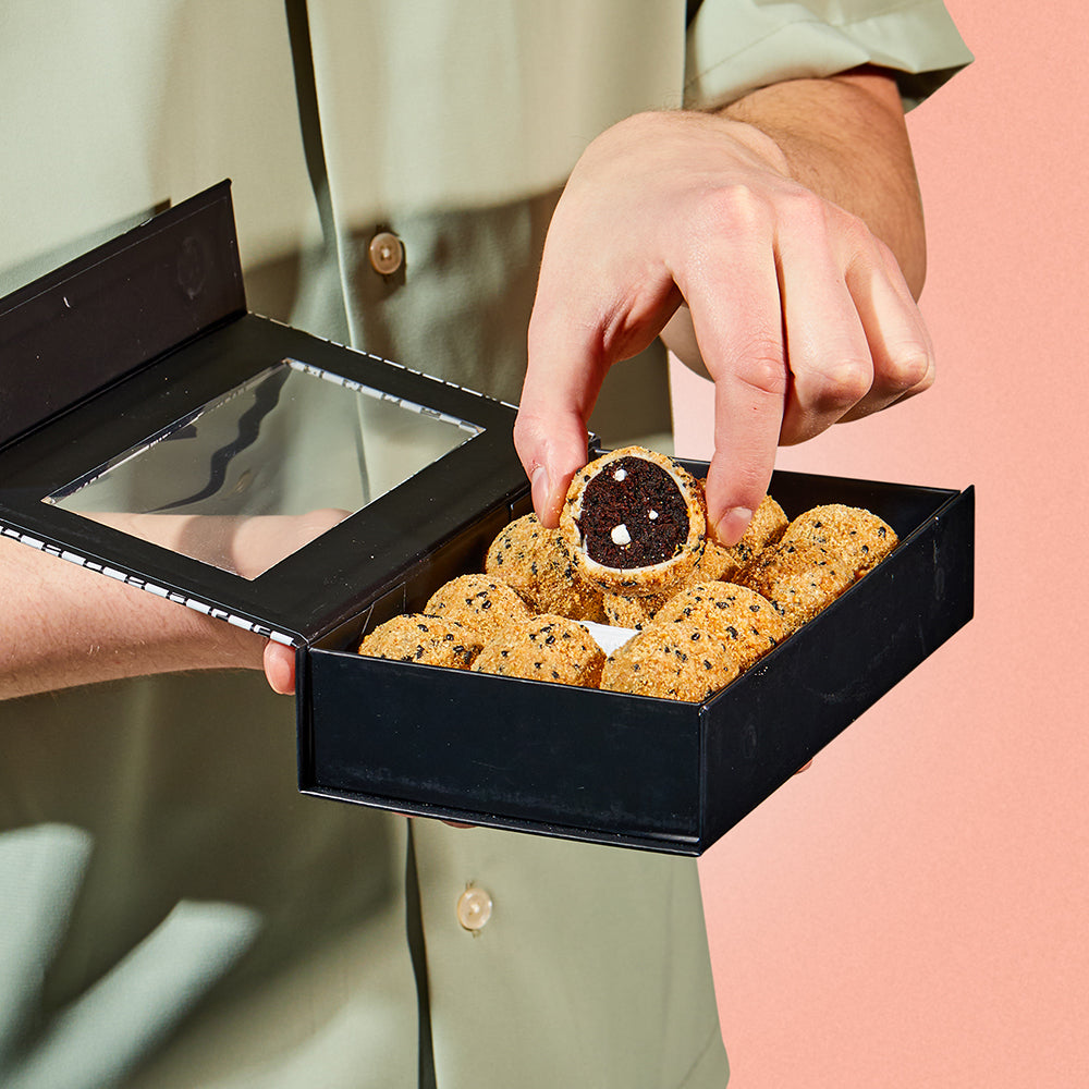 An open box of S'mores cake Truffles with a person's hand removing an individual truffle