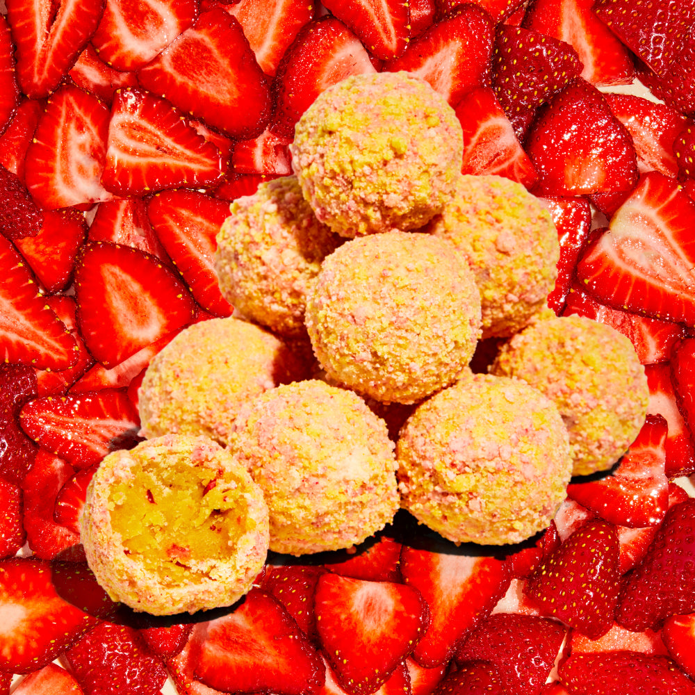 A pile of Strawberry Corn Cake truffles against a background of strawberries.