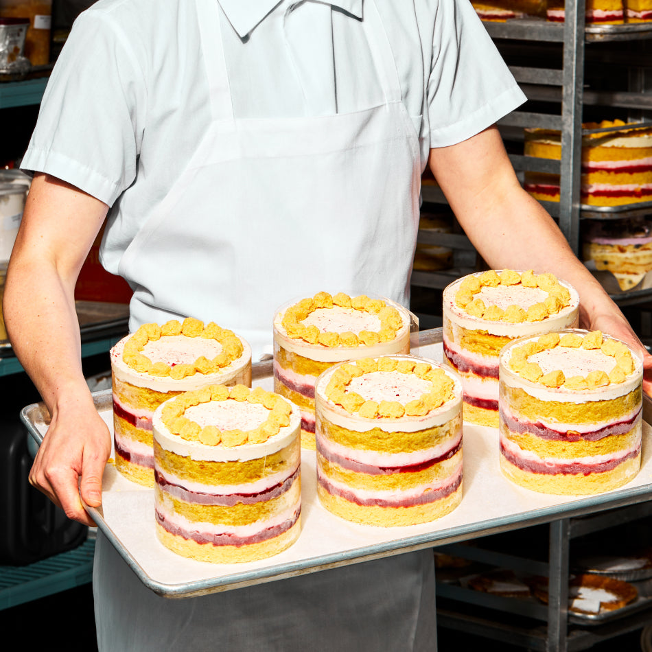 A baker holding a tray of 6 prepped Strawberry Corn Cakes