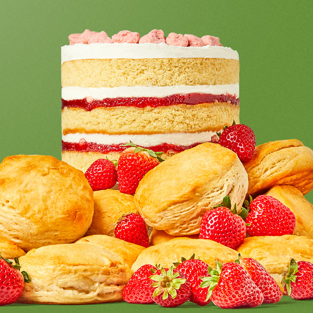 A 6 inch strawberry shortcake sitting on a pile of shortcake biscuits and strawberries.