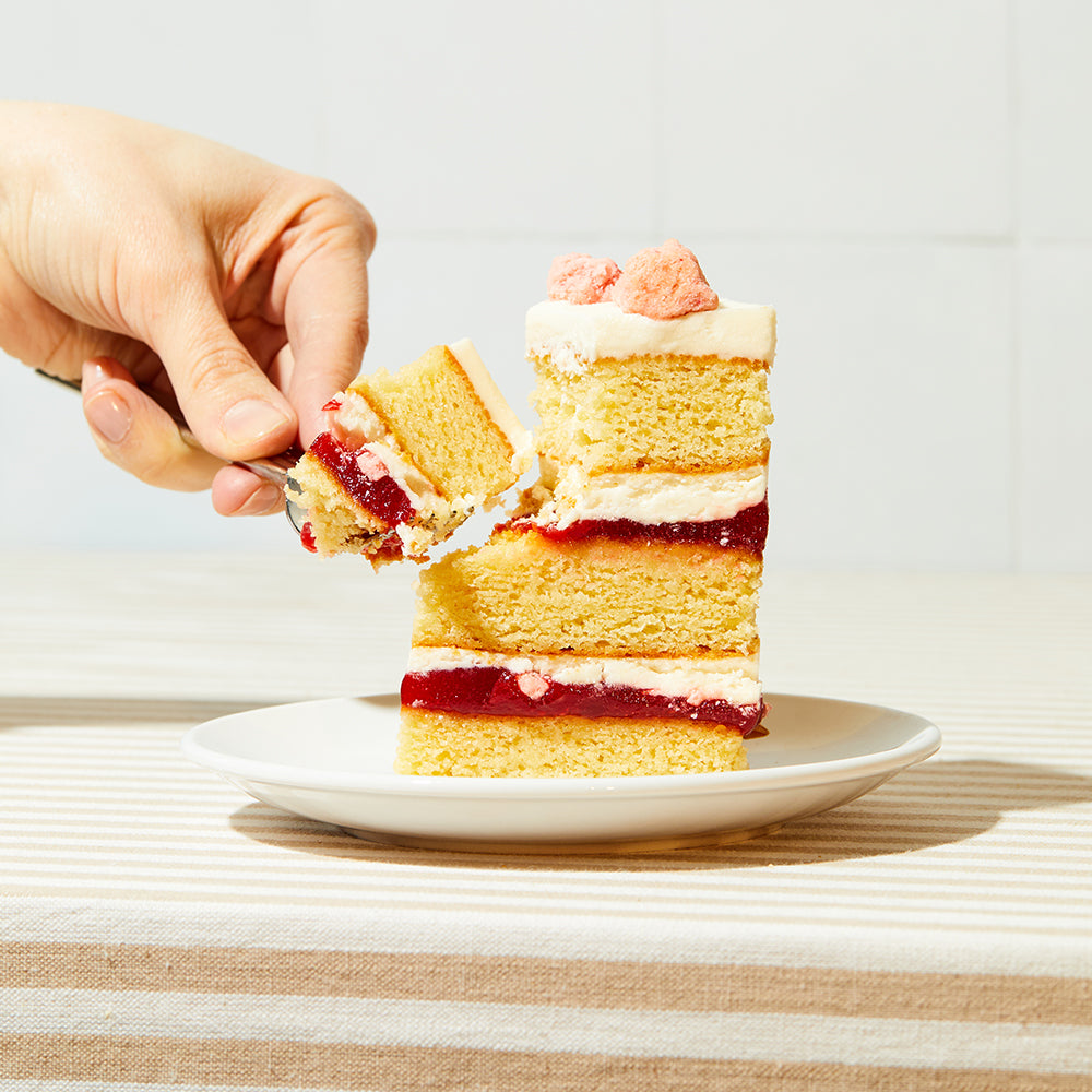 A fork removing a bite from a slice of strawberry shortcake cake on a small plate.