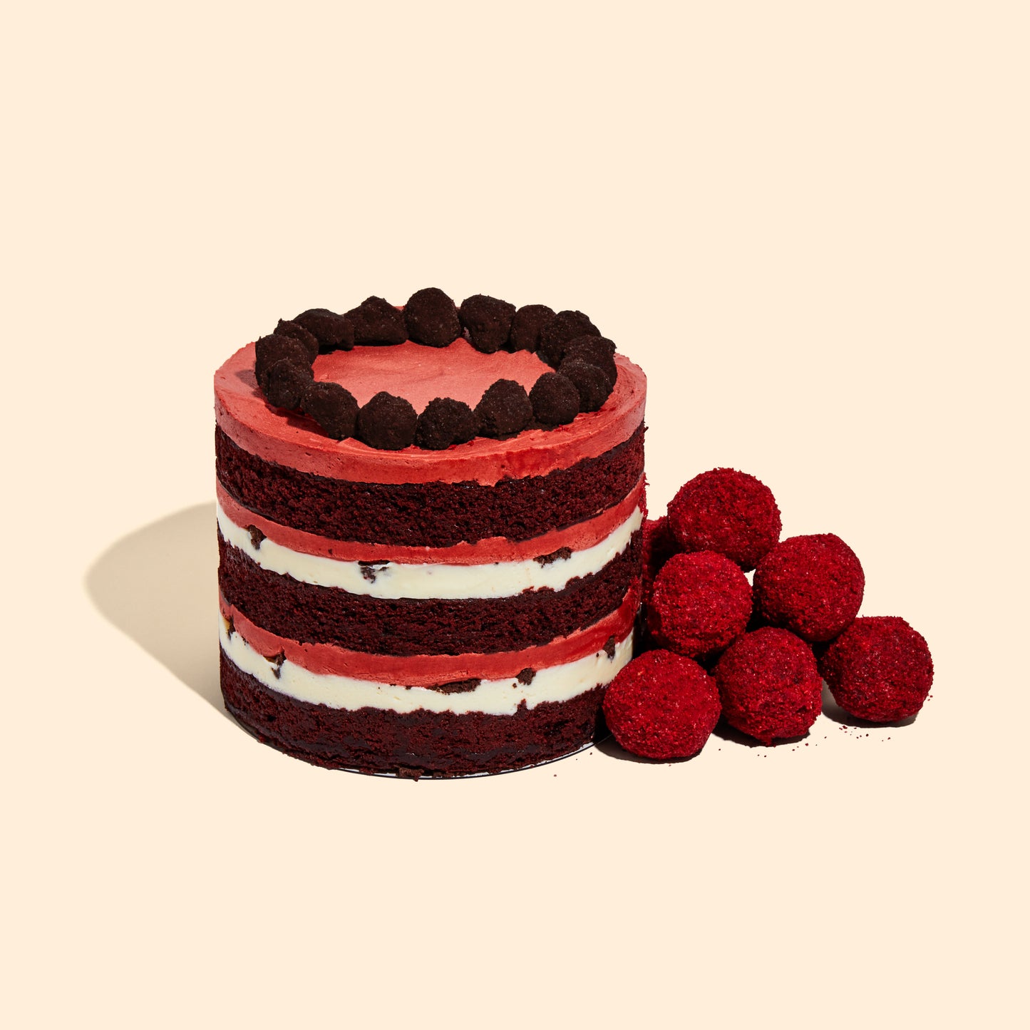 A pile of Red Velvet Cake Truffles sitting beside the 6" Red Velvet Cheesecake Cake.