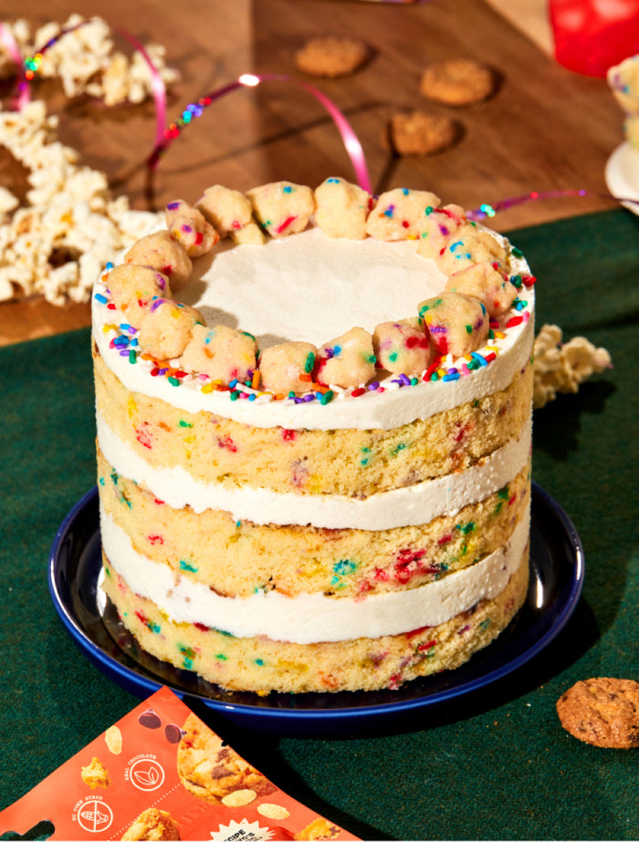 the fan favorite 6 inch birthday cake sitting on a festive dessert table surrounded by milk bar super crunchy cookies, popcorn, and sparkly string for gift wrapping