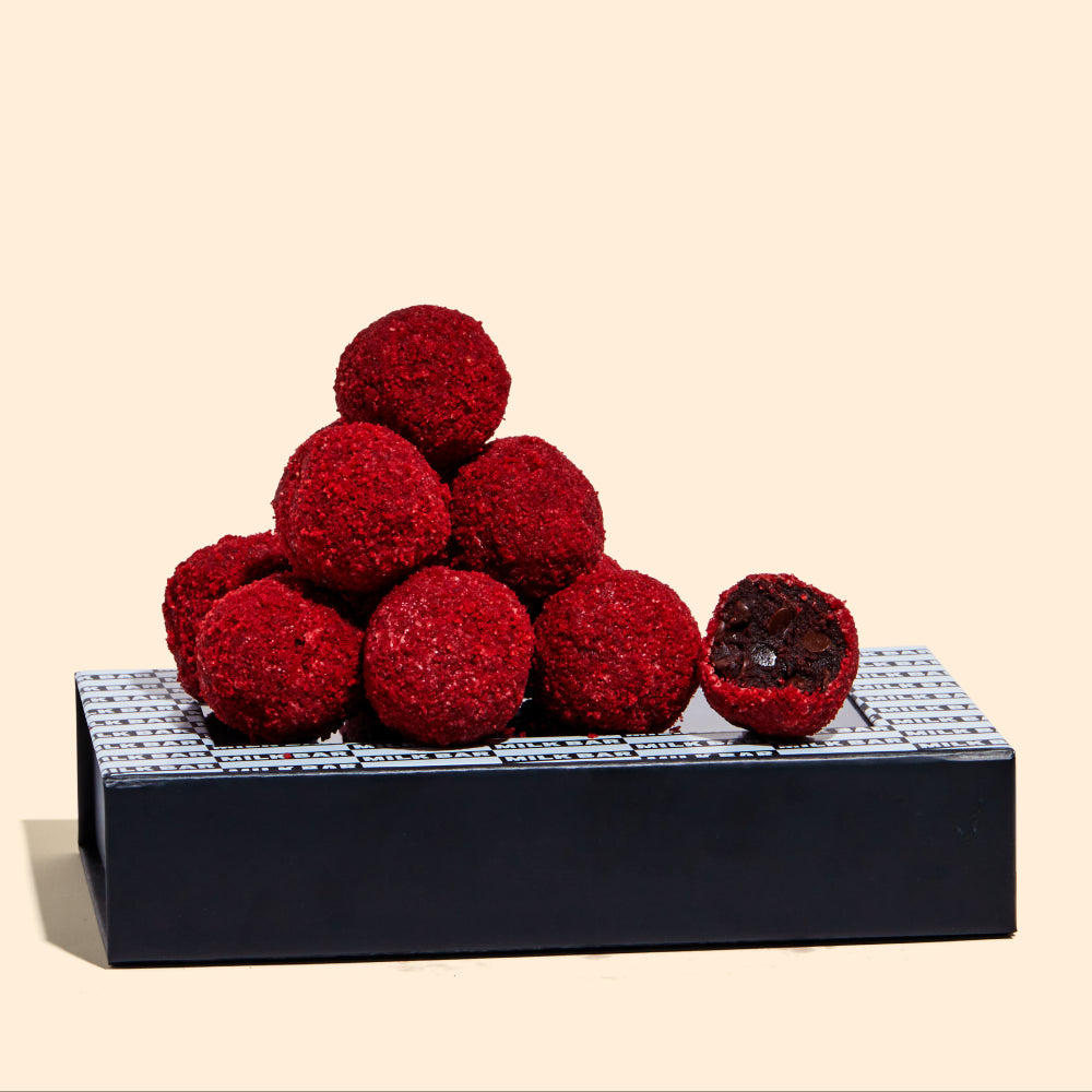 Side view of a Red Velvet Cheesecake Truffle Dozen box with a pile of truffles on top.