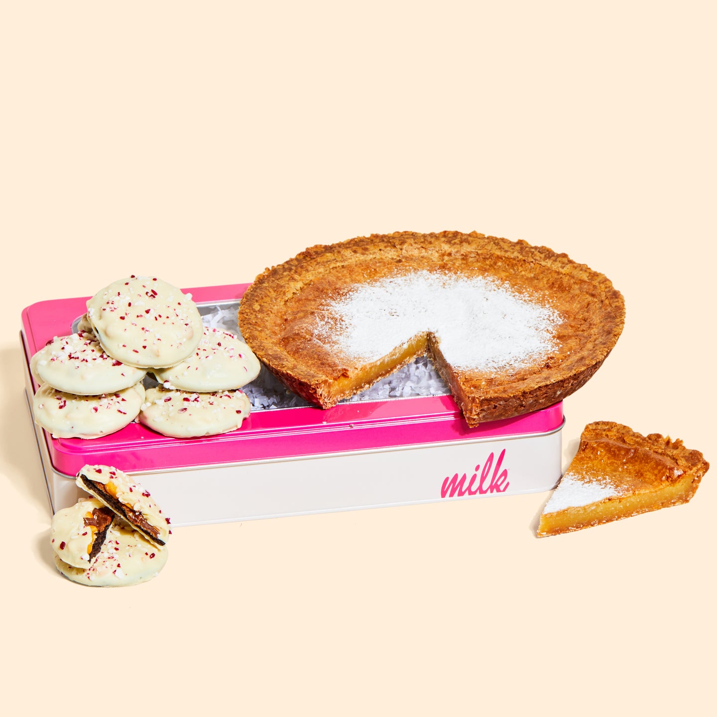 A stack of mini peppermint bark snap cookies on a branded milk bar tin, with a whole milk bar pie.