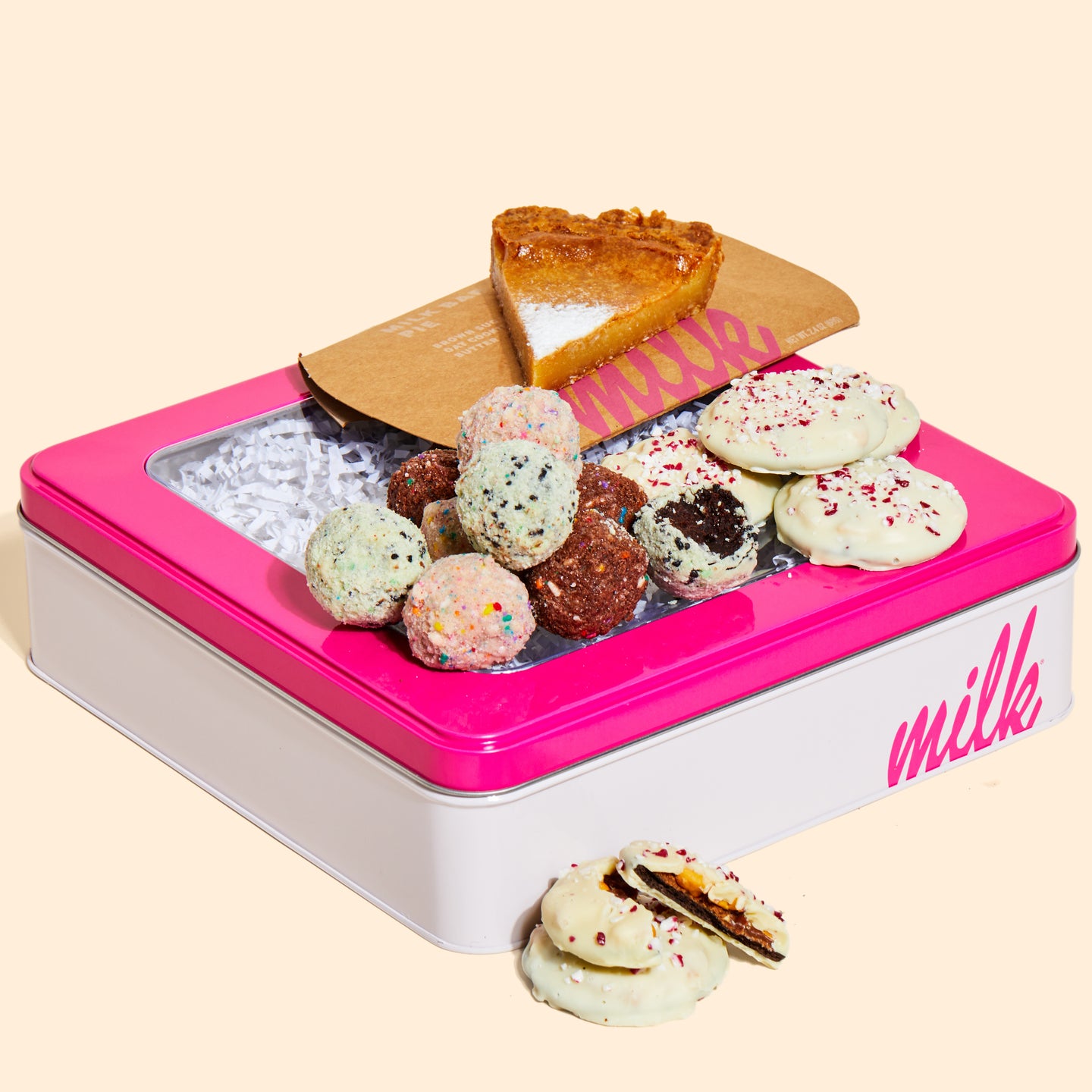 A slice of Milk Bar pie, pile of assorted truffles, and mini peppermint bark snap cookies sitting on top of a milk bar branded tin.